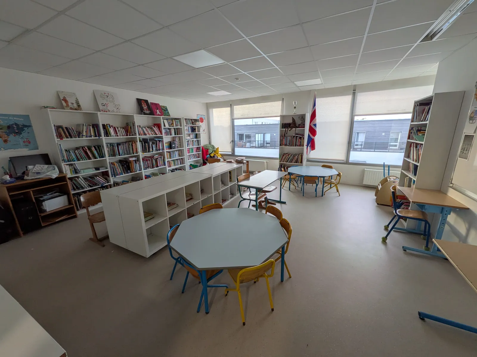 Rayonnages de livres le long des murs, meubles de rangement bas et tables rondes devant les fenêtres