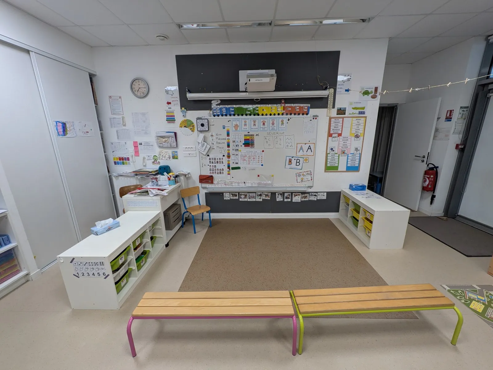 Deux bancs face à un tapis et au tableau d'affichage, entre deux meubles de rangement