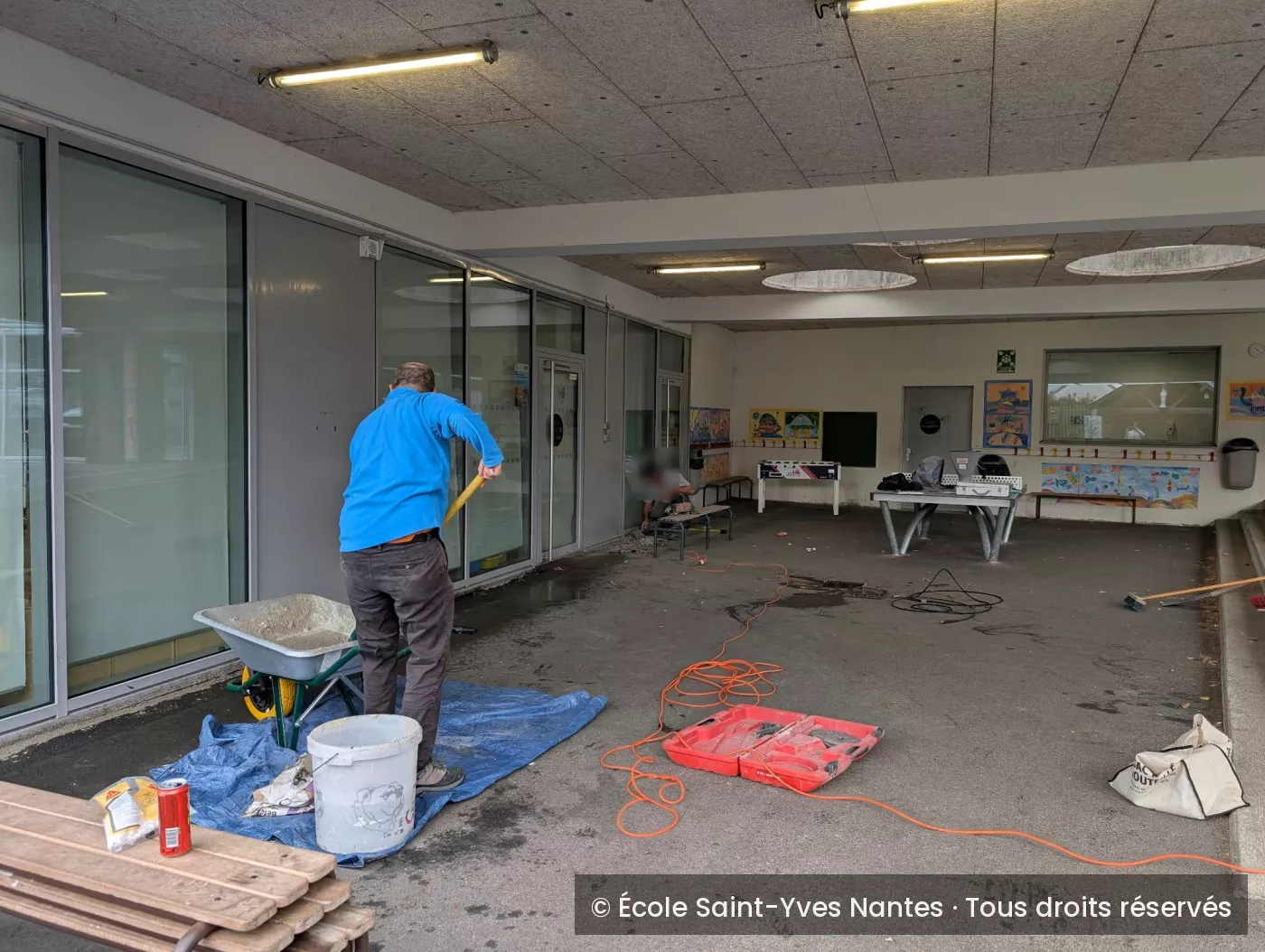 Parents au travail sous le préau, préparation du béton près d'une brouette